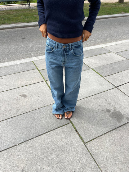 Vue rapprochée de la face avant du jean en denim bleu clair, mettant en valeur les passants pour ceinture, la fermeture éclair et le bouton.